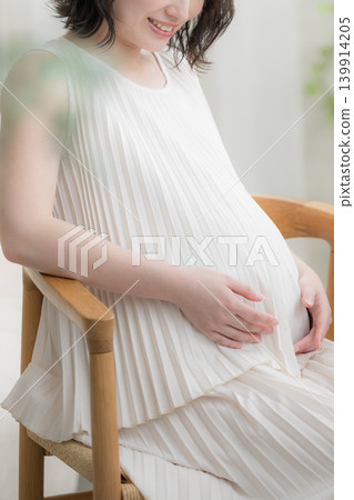 一位日本孕婦面帶微笑,將手放在肚子上;這張沒有臉的微笑照片代表了孕育生命的生活方式。 一位日本孕婦面帶微笑,將手放在肚子上;這張沒有臉的微笑照片代表了孕育生命的生活方式。 139914205