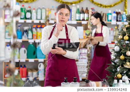 Female seller restocking using tablet while other is working in background Female seller restocking using tablet while other is working in background 139914248