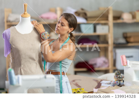 Dressmaker constructing custom dress on mannequin in sewing workshop Dressmaker constructing custom dress on mannequin in sewing workshop 139914328