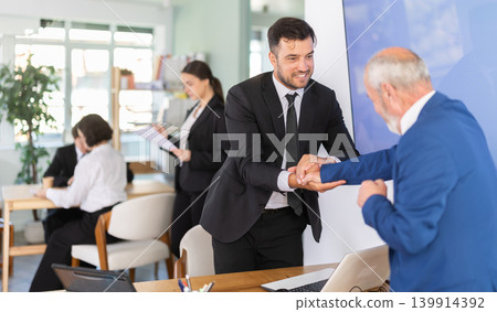 Professional adult male lawyer or bank clerk shaking hands with mature man client in bank office Professional adult male lawyer or bank clerk shaking hands with mature man client in bank office 139914392