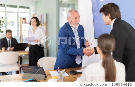 Elderly bank manager shaking hands with young couple customers Elderly bank manager shaking hands with young couple customers 139914418