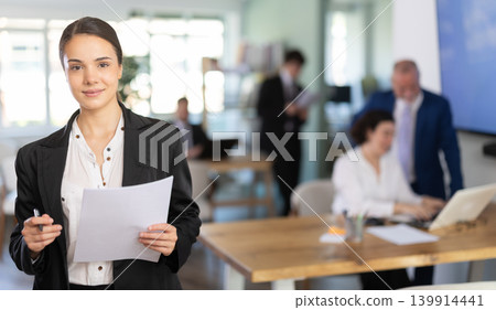 woman stands in the middle of a modern office and holds a job paper 139914441