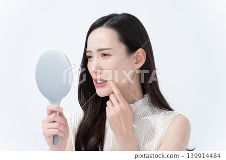A woman checks her skin in a hand mirror. A woman checks her skin in a hand mirror. 139914484