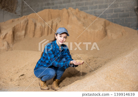 Female farmer holding handful of soybean hulls in farm storage Female farmer holding handful of soybean hulls in farm storage 139914639