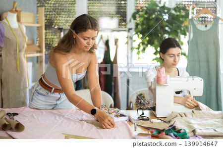 Female dressmaker cutting fabric next to assistant Female dressmaker cutting fabric next to assistant 139914647