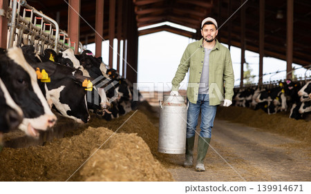 Man farmer carrying milk can in cowhouse Man farmer carrying milk can in cowhouse 139914671