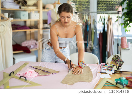 Young woman designer cutting fabric with scissors Young woman designer cutting fabric with scissors 139914826
