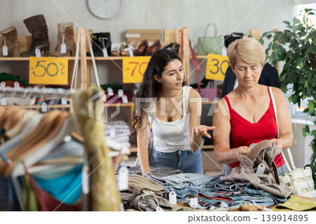 Armenian woman stands next to a mature woman near the counter in clothes store Armenian woman stands next to a mature woman near the counter in clothes store 139914895