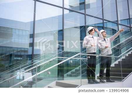 A full-body shot of a young construction worker, his supervisor, and his subordinate looking up at the future and their goals during a new employee training/talent development program. 139914906