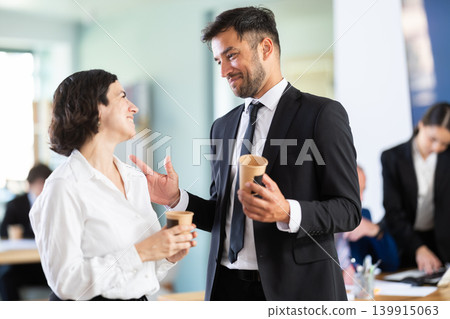 Adult man and woman colleagues drinking coffee in office Adult man and woman colleagues drinking coffee in office 139915063