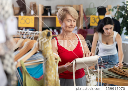Mature woman choosing a handbag in a store Mature woman choosing a handbag in a store 139915070