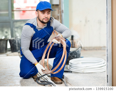 Portrait of a young builder with a coil of heating cable Portrait of a young builder with a coil of heating cable 139915100