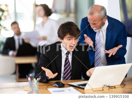 Strict mature man boss scolding young guy office worker for improper operation on laptop in office 139915108