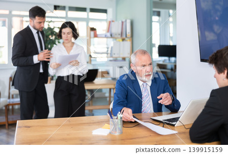 Experienced mature male bank manager talking with man client and helping opening account in bank at office Experienced mature male bank manager talking with man client and helping opening account in bank at office 139915159