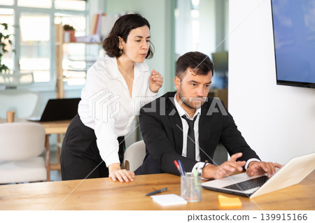 Focused young female business worker helping male colleague with laptop, discussing new project in office Focused young female business worker helping male colleague with laptop, discussing new project in office 139915166