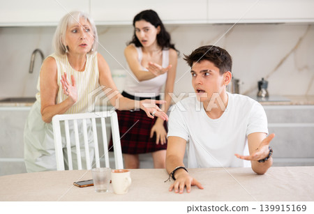 Upset and unhappy son-in-law sitting in the kitchen separately, family conflict Upset and unhappy son-in-law sitting in the kitchen separately, family conflict 139915169