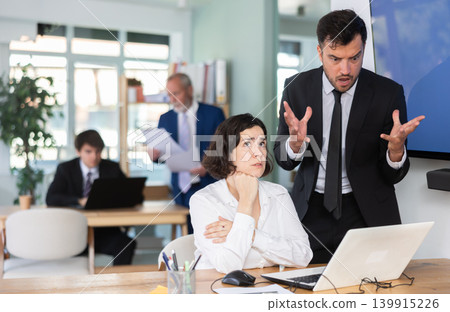 Strict adult man boss scolding new young girl co-worker for mistakes in working on laptop in office 139915226