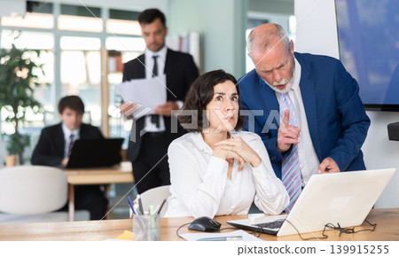 Strict mature man boss scolding girl office worker for improper operation on laptop in office Strict mature man boss scolding girl office worker for improper operation on laptop in office 139915255