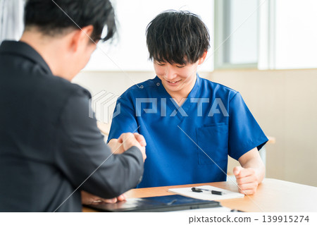 A businessman from a medical equipment manufacturer and a doctor in a scrub shaking hands A businessman from a medical equipment manufacturer and a doctor in a scrub shaking hands 139915274