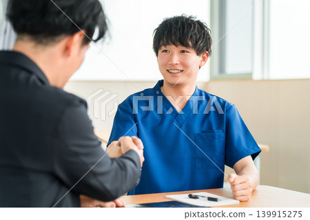 A businessman from a medical equipment manufacturer and a doctor in a scrub shaking hands A businessman from a medical equipment manufacturer and a doctor in a scrub shaking hands 139915275