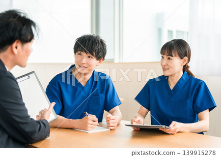一位來自醫療設備製造商的男性商人和一位穿著手術服的男性和女性醫務人員正在進行銷售和商業談判 一位來自醫療設備製造商的男性商人和一位穿著手術服的男性和女性醫務人員正在進行銷售和商業談判 139915278