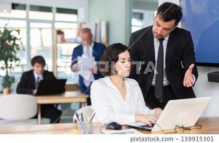 Adult man helping adult female colleague work on laptop Adult man helping adult female colleague work on laptop 139915301