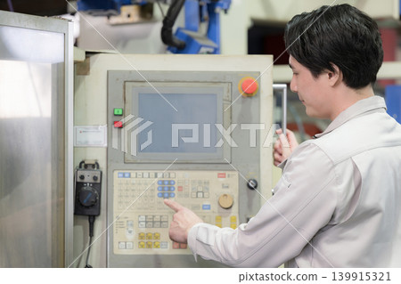 畫面展示了一名年輕工人在工廠或生產現場操作設備,以及生產管理。點擊面板。 畫面展示了一名年輕工人在工廠或生產現場操作設備,以及生產管理。點擊面板。 139915321