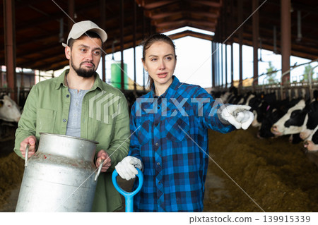Man and woman farmers standing in cowshed and talking Man and woman farmers standing in cowshed and talking 139915339