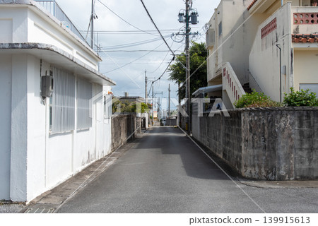 A sunny street alleyway where the shadows of utility poles and houses fall on the road. A sunny street alleyway where the shadows of utility poles and houses fall on the road. 139915613