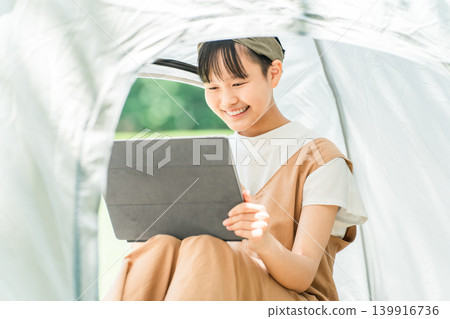 一名女孩在露營地/休閒設施的帳篷內使用平板電腦。 一名女孩在露營地/休閒設施的帳篷內使用平板電腦。 139916736