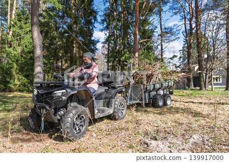 Woman driving ATV quad bike with trailer full of firewood in forest in Estonia, Europe Woman driving ATV quad bike with trailer full of firewood in forest in Estonia, Europe 139917000