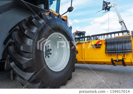 Close-up of a tractor tire and yellow agricultural machinery on display at a trade show Close-up of a tractor tire and yellow agricultural machinery on display at a trade show 139917014