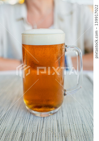 Refreshing mug of golden beer with foam head, served cold on a table outdoors, isolated Refreshing mug of golden beer with foam head, served cold on a table outdoors, isolated 139917022