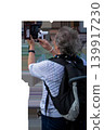 An elderly woman with a backpack from behind taking a photo with a smartphone in a wallet case on an isolated transparent background. High quality photo 139917230