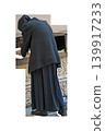 Elderly orthodox nun or pilgrim walking isolated on transparent background. Back view of senior christian woman in black habit, headscarf and long dress. Monastery lifestyle and cathedral cutout 139917233
