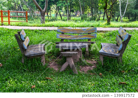 Traditional stone park benches and table with painted wood imitation texture surrounded by green grass in a summer garden Traditional stone park benches and table with painted wood imitation texture surrounded by green grass in a summer garden 139917572