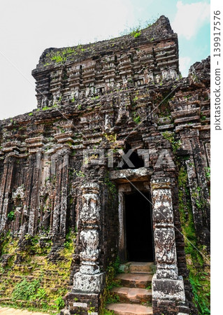 Ancient ruined red brick Hindu temple tower with decorated columns and dark stone doorway at My Son Sanctuary in Vietnam Ancient ruined red brick Hindu temple tower with decorated columns and dark stone doorway at My Son Sanctuary in Vietnam 139917576
