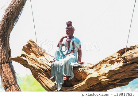Beautiful Guanyin Bodhisattva statue sitting on driftwood swing inside a woven vine circle frame in Vietnam garden 139917623