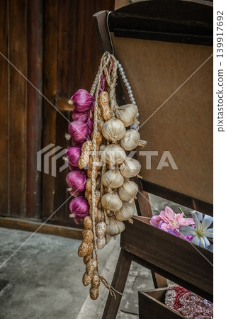 Decorative bundles of artificial purple onion garlic bulbs and peanuts hanging on a wooden chair outdoors Decorative bundles of artificial purple onion garlic bulbs and peanuts hanging on a wooden chair outdoors 139917692