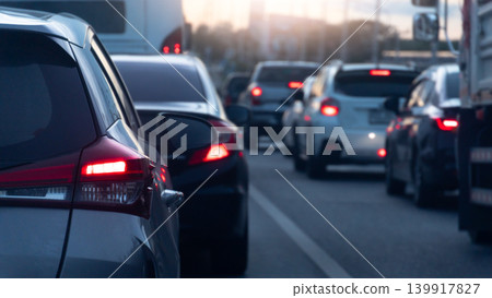 Perspective from between cars gridlocked in a multi-lane traffic jam during twilight. Bright red tail lights glow intensely against the darkening evening atmosphere on a busy highway. Perspective from between cars gridlocked in a multi-lane traffic jam during twilight. Bright red tail lights glow intensely against the darkening evening atmosphere on a busy highway. 139917827