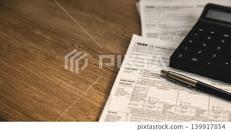 Calculator and pen placed on individual income tax return form with copy space on wooden desk for tax calculation, accounting review, financial reporting, and budget management workflow. Calculator and pen placed on individual income tax return form with copy space on wooden desk for tax calculation, accounting review, financial reporting, and budget management workflow. 139917854