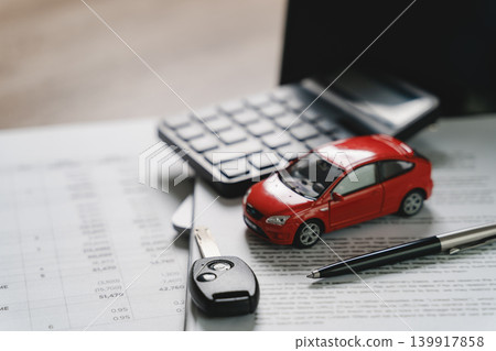 Red car model with calculator, vehicle key, pen, and financial documents on office desk representing car financing, auto loan calculation, insurance payment, and automobile ownership process. 139917858