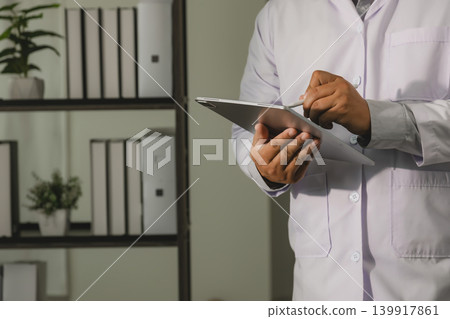 Doctor using tablet with stylus in medical office for healthcare research, digital communication, patient information management, online consultation, and clinical workflow process. Doctor using tablet with stylus in medical office for healthcare research, digital communication, patient information management, online consultation, and clinical workflow process. 139917861