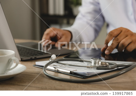 Doctor working on tablet beside stethoscope and medical documents in healthcare office for digital consultation, patient management, medical communication, and clinical workflow process. Doctor working on tablet beside stethoscope and medical documents in healthcare office for digital consultation, patient management, medical communication, and clinical workflow process. 139917865