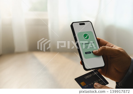 Hand holding smartphone with completed mobile payment transaction and credit card during online banking process for digital finance, banking, transfer, and secure payment management. Hand holding smartphone with completed mobile payment transaction and credit card during online banking process for digital finance, banking, transfer, and secure payment management. 139917872