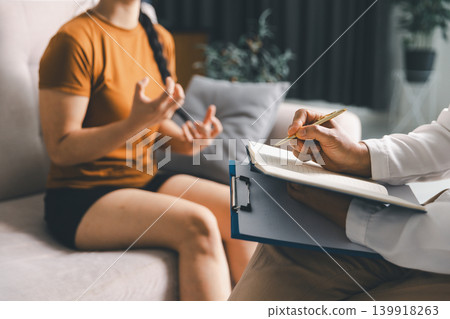 Close up of young woman expressing emotions with hand gestures during mental health counseling session while therapist takes notes, symbolizing psychotherapy, communication, support, trust, recovery. Close up of young woman expressing emotions with hand gestures during mental health counseling session while therapist takes notes, symbolizing psychotherapy, communication, support, trust, recovery. 139918263