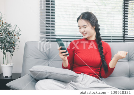 Young Asian woman smiling at smartphone on sofa at home, checking online shopping app or mobile notification, digital consumer lifestyle, ecommerce browsing, good news and convenient home technology Young Asian woman smiling at smartphone on sofa at home, checking online shopping app or mobile notification, digital consumer lifestyle, ecommerce browsing, good news and convenient home technology 139918321