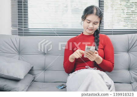 Young Asian woman using smartphone for online shopping at home, browsing ecommerce app on sofa with credit card nearby, mobile payment, cashless lifestyle and digital consumer concept Young Asian woman using smartphone for online shopping at home, browsing ecommerce app on sofa with credit card nearby, mobile payment, cashless lifestyle and digital consumer concept 139918323