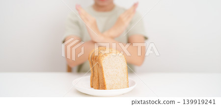 Unhappy woman showing Rejecting gesture and refusing to eat bread. concept of gluten intolerance, gluten sensitivity, carb loading concerns, or a disliking for unhealthy dietary habits Unhappy woman showing Rejecting gesture and refusing to eat bread. concept of gluten intolerance, gluten sensitivity, carb loading concerns, or a disliking for unhealthy dietary habits 139919241