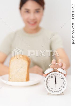 Happy smiling woman with whole wheat bread and alarm clock. concept of intermittent fasting, IF, meal timing, and choosing healthy carbohydrates for a balanced diet and weight loss management Happy smiling woman with whole wheat bread and alarm clock. concept of intermittent fasting, IF, meal timing, and choosing healthy carbohydrates for a balanced diet and weight loss management 139919245